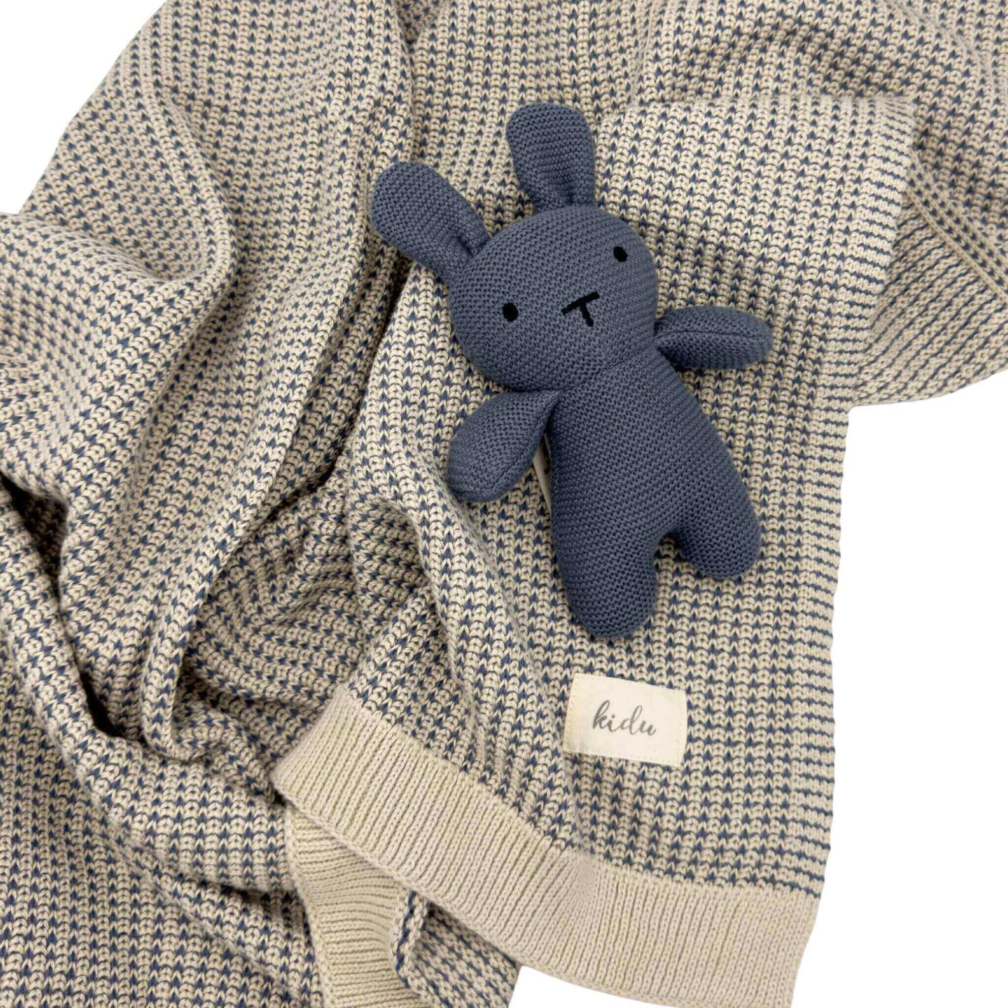 baby Blue knitted bunny toy on a textured beige and blue blanket with a visible kidu brand label.